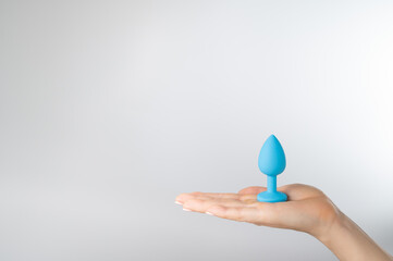 Woman holding a blue anal plug on a white background. Adult toy for alternative sex