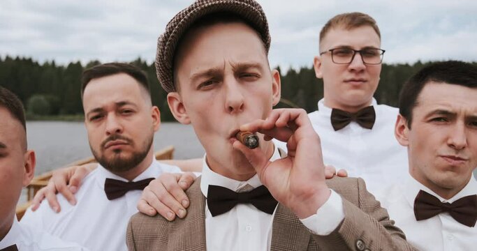 Men's band, group of gangsters friends, cool guys looking at camera. A man boss is smoking cigar, exhales smoke in the camera. Gang of serious men with leader or ringleader.
