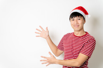 Happy young adult Asian man with Christmas theme t-shirt, Christmas hat or Santa's hat show hands on empty copy space for texting or advertisement on isolated white background. Asian Christmas concept