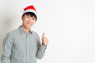 Happy young adult Asian man with Christmas theme shirt, Christmas hat or Santa's hat show thumbs up on copy space for texting or advertisement on isolated white background. Asian Christmas concept.