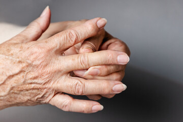 A senior woman massages her fingers, experiencing pain in the joints. Gray background, hands...