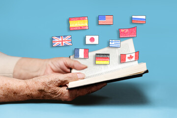 Education. A senior woman reading a book with flags of different countries. Close up. Blue...