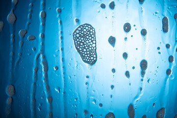 Water drops with foam on glass on a blue background.