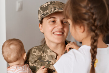 Closeup portrait of smiling optimistic military mother wearing camouflage uniform and hat, meeting...