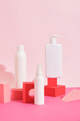 several different white plastic bottles and tube on pink geometric podiums on pink background