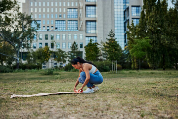 Fototapeta premium Asian woman unrolling yoga mat for doing yoga in park