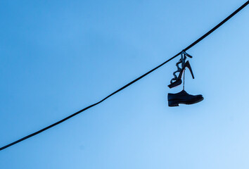 Mans and female classic shoes hanging on the electric wire against blue sky