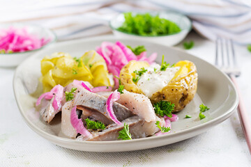 Herring with baked potato, onions and pickled cucumber on a plate. Traditional cuisine.