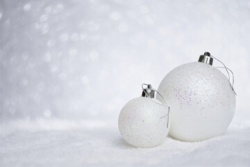 Merry Christmas Card. Christmas bright balls on the snow with copy space. Two white glittering baubles on bokeh background. Merry Christmas and Happy New Year concept.