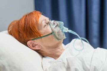 Close-up of senior woman patient receiving oxygen mask lying on a hospital bed during pandemic at...