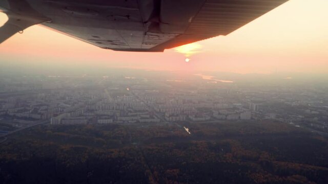 A propeller plane is flying above a village or a small town during a sunset and golden hour, beautiful landscape and nice weather, passenger point of view, smooth shot, cinematic shot