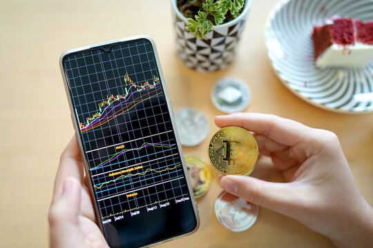 Maesot, Thailand- June 13, 2021:Hand of woman's holding Bitcoin and smartphone showing stock chart in cafe. Concept crypto currency virtual money.