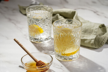 Two glasses with water and lemon, honey in the morning light - breakfast
