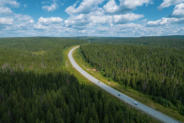 Aerial view of scenic road between green trees with pines on a sunny summer morning. Nature landscape in Siberia, Russia. A road passing through a coniferous forest, aerial shot from a drone.