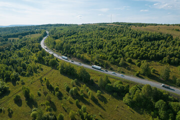 Fototapeta na wymiar Aerial view of scenic road between green trees with pines on a sunny summer morning. Nature landscape in Siberia, Russia. A road passing through a coniferous forest, aerial shot from a drone.