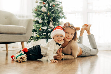 Obraz na płótnie Canvas Portrait of two charming children in Christmas costumes next to the Christmas tree on the eve of the holidays. Festive mood, positive emotions. Christmas and New Year