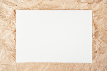 Background image crumpled recycled textured kraft paper with sheet of white cardboard in middle. Top view. Copy space