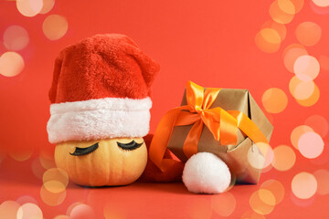 wrapped christmas gifts and pumpkin in santa hat and false eyelashes on red background