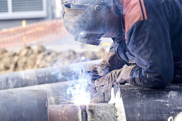 Construction worker arc welding the metal pipe.