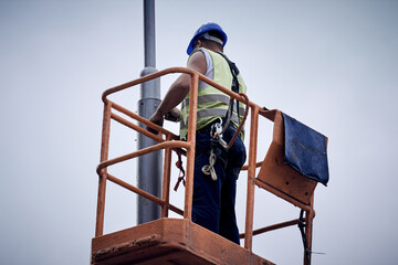 Manual worker on a telescopic lifter basket fixing street light pole.