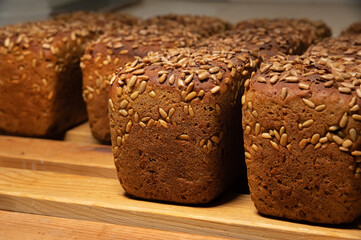 A lot of whole delicious homemade rectangular rye bread with sunflower seeds on top lies on a wooden rack background
