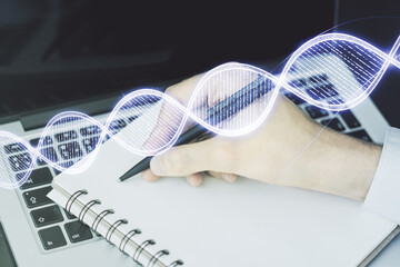 Double exposure of creative DNA hologram and hand writing in notebook on background with laptop. Bio Engineering and DNA Research concept