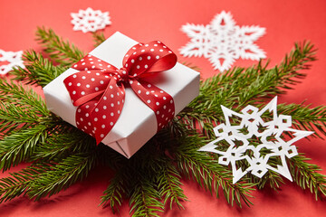 Gift box with Christmas tree branch and white snowflakes on red