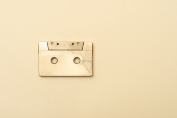 Gold fancy retro old audio cassette tape on beige color background. Retro mixtape, 1980s pop songs...