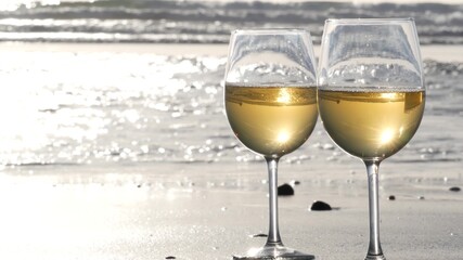Two wineglasses on sandy ocean beach. Couple of glasses and pebbles, white wine for romantic date near sea water. Cozy beachfront sunset near tide waves. Seamless looped cinemagraph. California, USA.