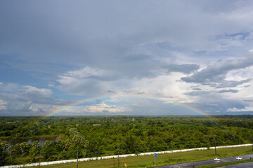 Rainbow over the lake and the forest on blue sky and white clouds background.Landscape rainbow in the country side.