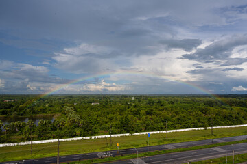 Rainbow over the lake and the forest on blue sky and white clouds background.Landscape rainbow in the country side.