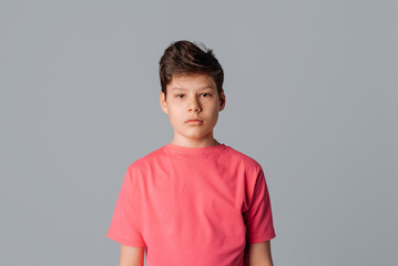 Teenager boy wearing casual pink t shirt standing over gray isolated background, looking at the camera
