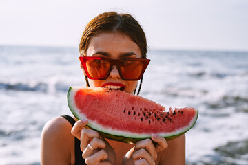 cheerful woman in sunglasses eating watermelon by the ocean