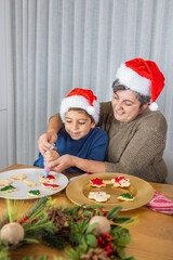 Little kid and his grandmother decorating christmas cookies at home