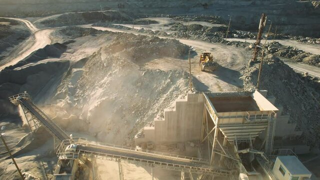 Arial view of the open pit mine. Front end loader loading sand into stone jaw crusher in open-pit. Heavy machinery working in quarry. Development opencast for mining minerals