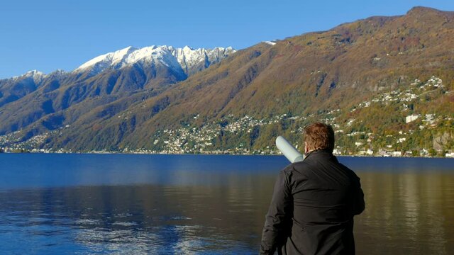 Man Using a Telescope to Looking at Alpine Lake Maggiore with Snow-capped Mountain in a Sunny Autumn Day in Ascona, Ticino in Switzerland.