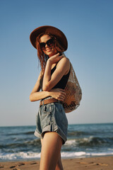 cheerful woman in a hat with sunglasses walking with a bag