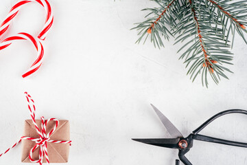 Christmas gift box and scissors on white concrete background with branch of Christmas tree. Top...