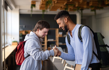 Young happy man with Down syndrome with his mentoring friend greeting indoors at school.