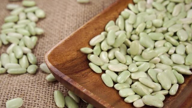 Green organic verdina beans falling into wooden kitchenware on rustic burlap in slow motion. Dried legumes close up. Traditional Spanish Mediterranean cuisine concept. Asturias region