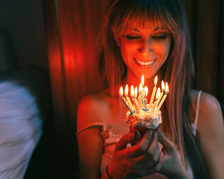 Smiling woman looking at cupcake with burning candles on birthday