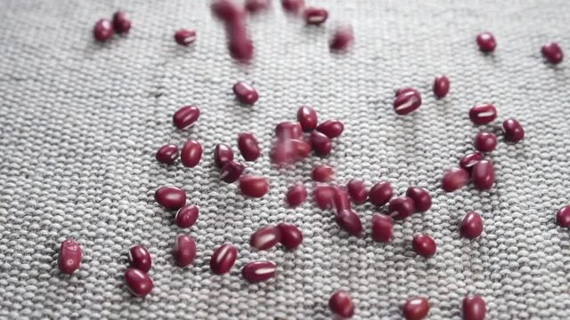 Red adzuki or azuki beans. Falling uncooked organic legume grains on a rough jute rustic cloth in slow motion. Close up. Traditional Japanese food