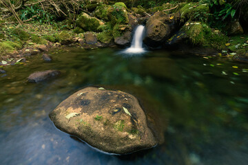 A small waterfall on a mountain river flowing through some stones with a big rock in the foreground
