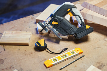 building level, tape measure and jigsaw lie on the desktop among the boards
