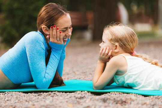 Smiling mother and daughter looking at each other while lying on exercise mat