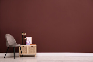 Stylish commode and armchair near brown wall, space for text