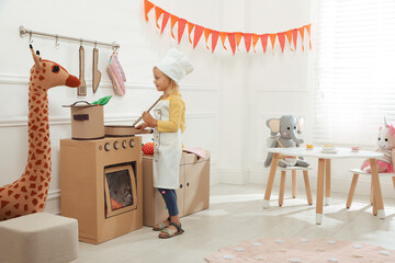 Little girl playing with toy cardboard kitchen at home