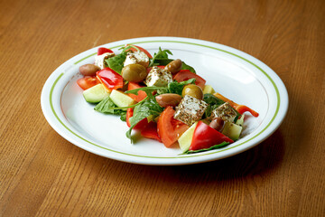 Appetizing vegetable salad with feta and olives in a white plate on a wooden background