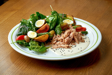 Salad with tuna, potatoes, eggs and onions in a white plate. Nicoise salad