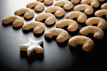 A cinnamon star and several vanilla cookies on black background.